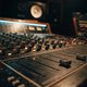 A moody, close-up shot of a professional mixing desk in a dimly lit studio, focusing on the faders and knobs for the bass channel, with subtle monitor speaker reflections in the background. No screens or plugin UIs are visible.