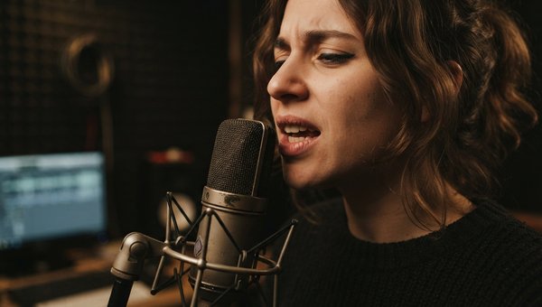 Close-up shot of a singer's mouth near a vintage condenser microphone in a dimly lit, professional studio, conveying focus and emotion. Soft, warm lighting.